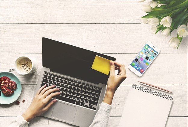 woman's hands placing sticky-note on screen of laptop computer; sitting at home desk