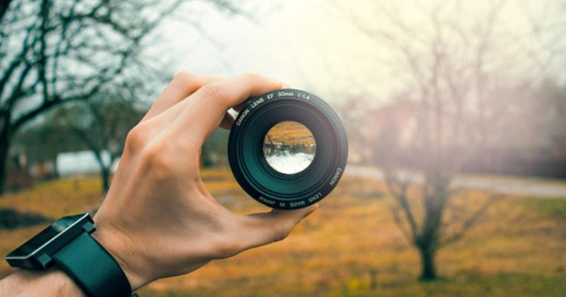 hand holding a focus lens on a camera focused on outdoor scene