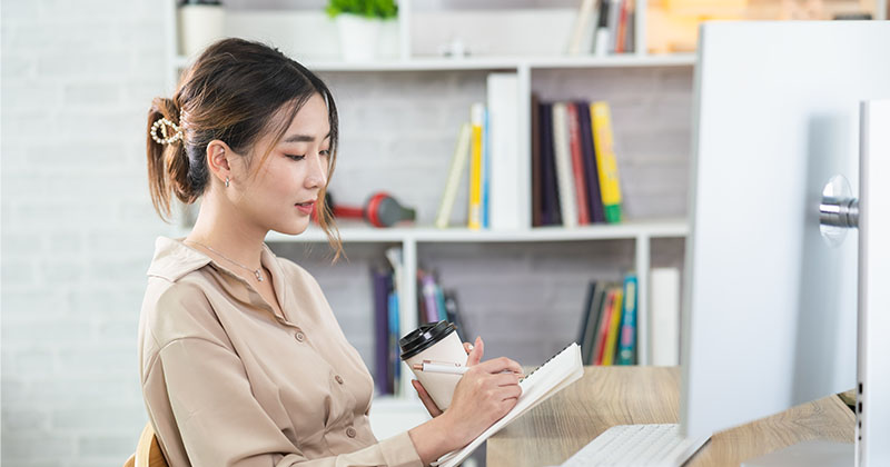 woman writing notes by computer; working from home online