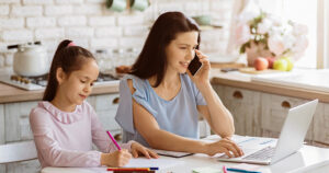 mom at work on laptop with daughter beside her colouring