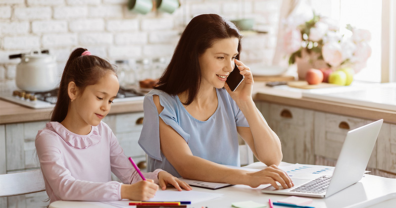 mom at work on laptop with daughter beside her colouring